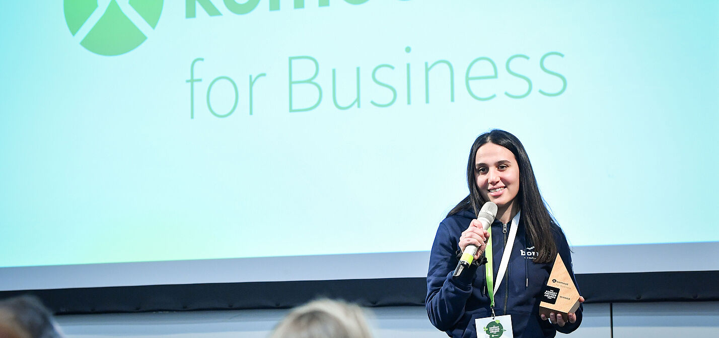 2025_komoot-Partner-Awards-2024-Vergabe-Rede_Gabriele-Giessenboeck Frau redet in Mikrofon mit komoot Partner Award 2024 in der Hand