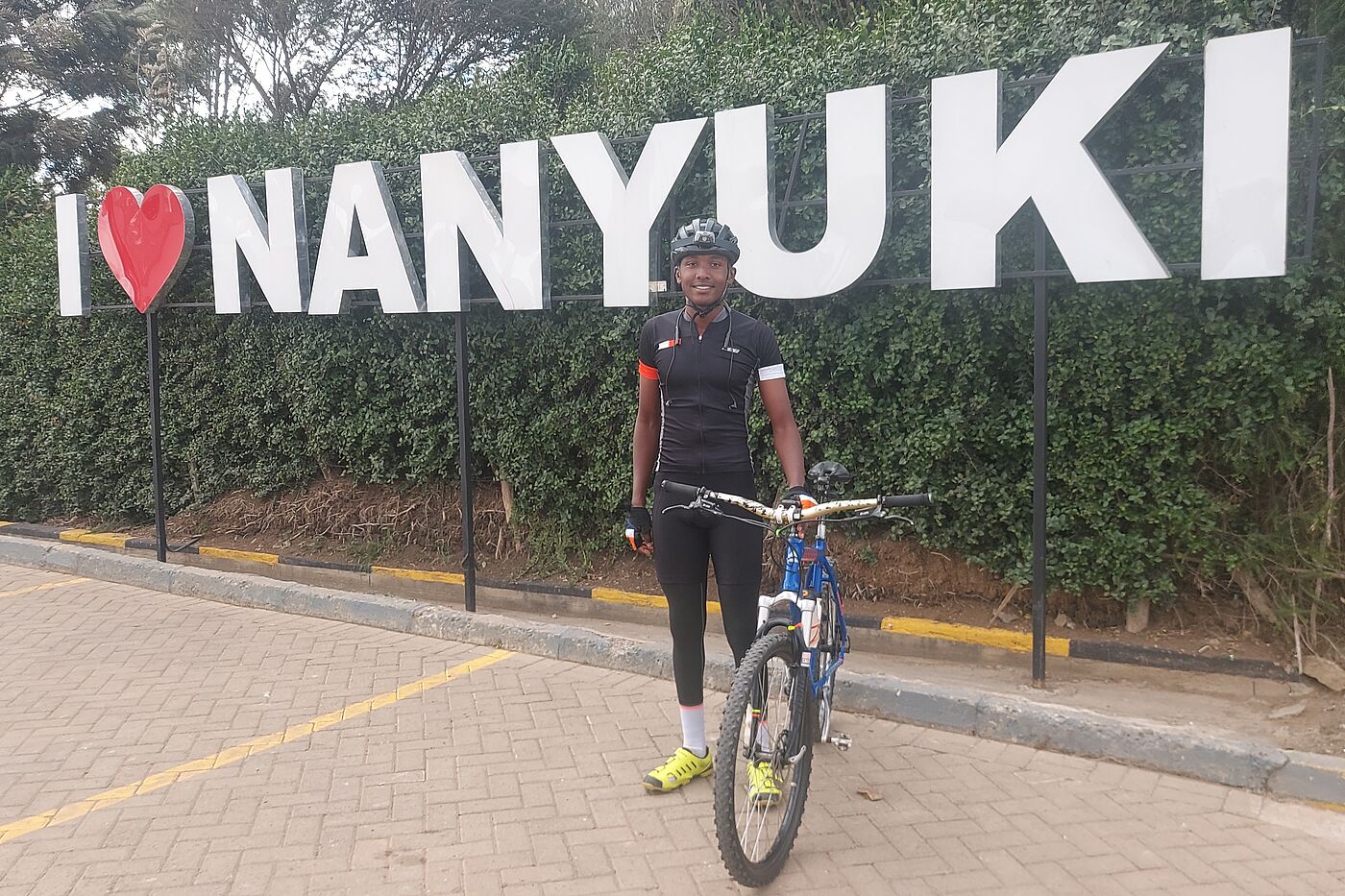 James Nanyui Radfahrer vor Plakat I love Nanyuki