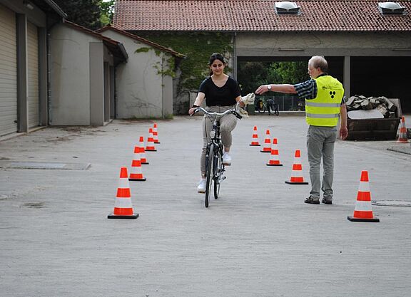 Übung Radfahrschule Frau fährt mit Fahrrad und nimmt Tuch von Lehrer entgegen