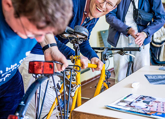 Junger ADFC Menschen reparieren gemeinsam ein gelbes Fahrrad und lachen.