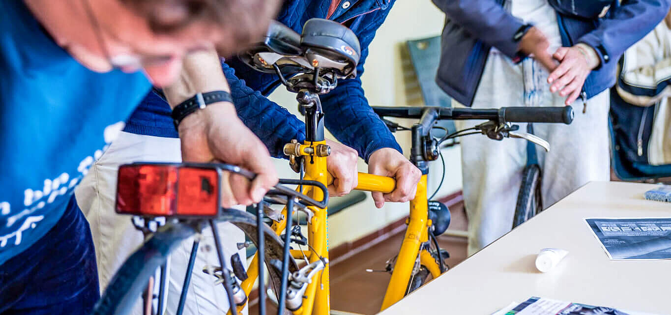 Menschen reparieren gemeinsam ein gelbes Fahrrad und lachen.